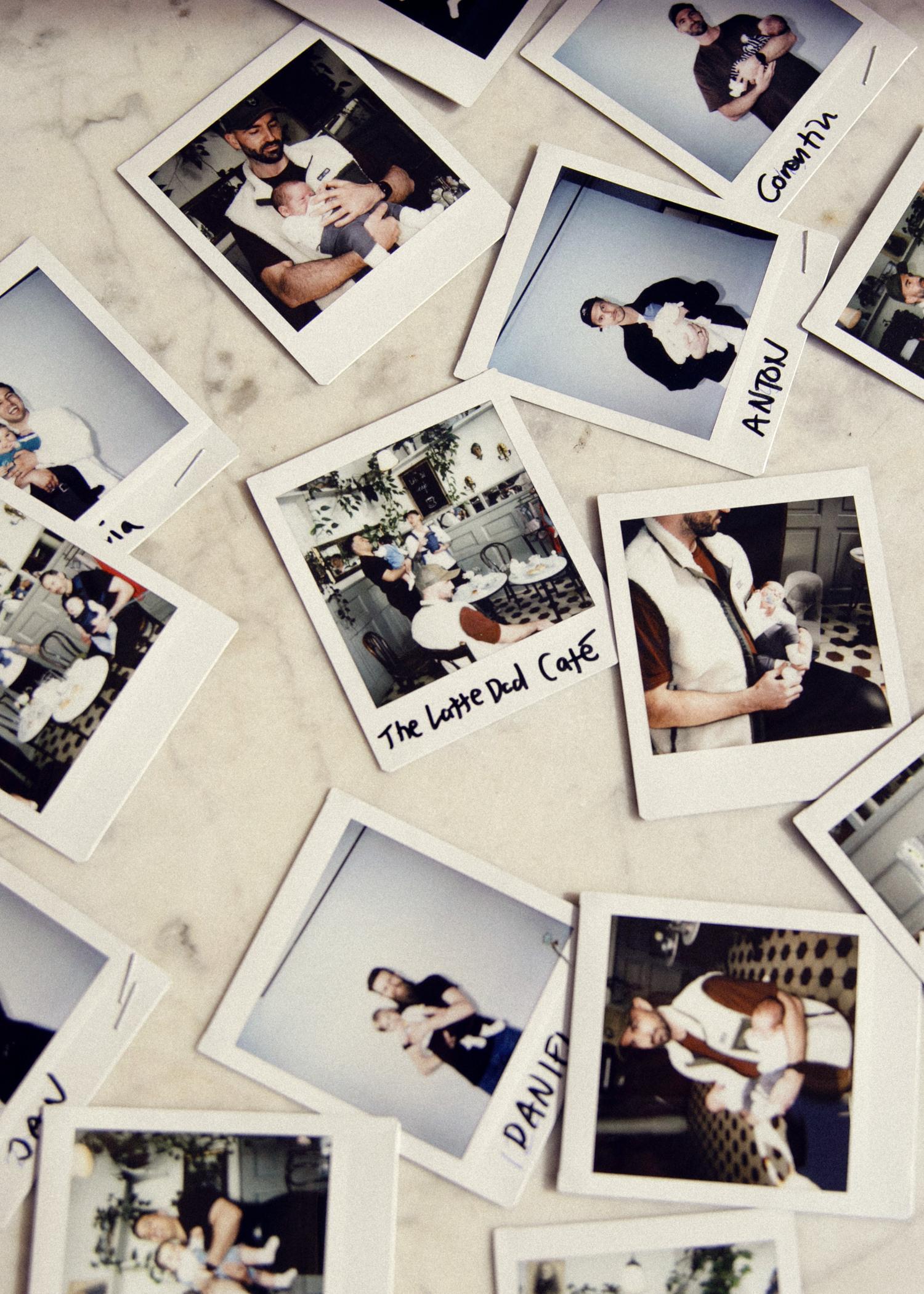 Scattered Polaroid photos of people holding babies, some labeled with names and "The Latte Dad Café," laid out on a marble surface.